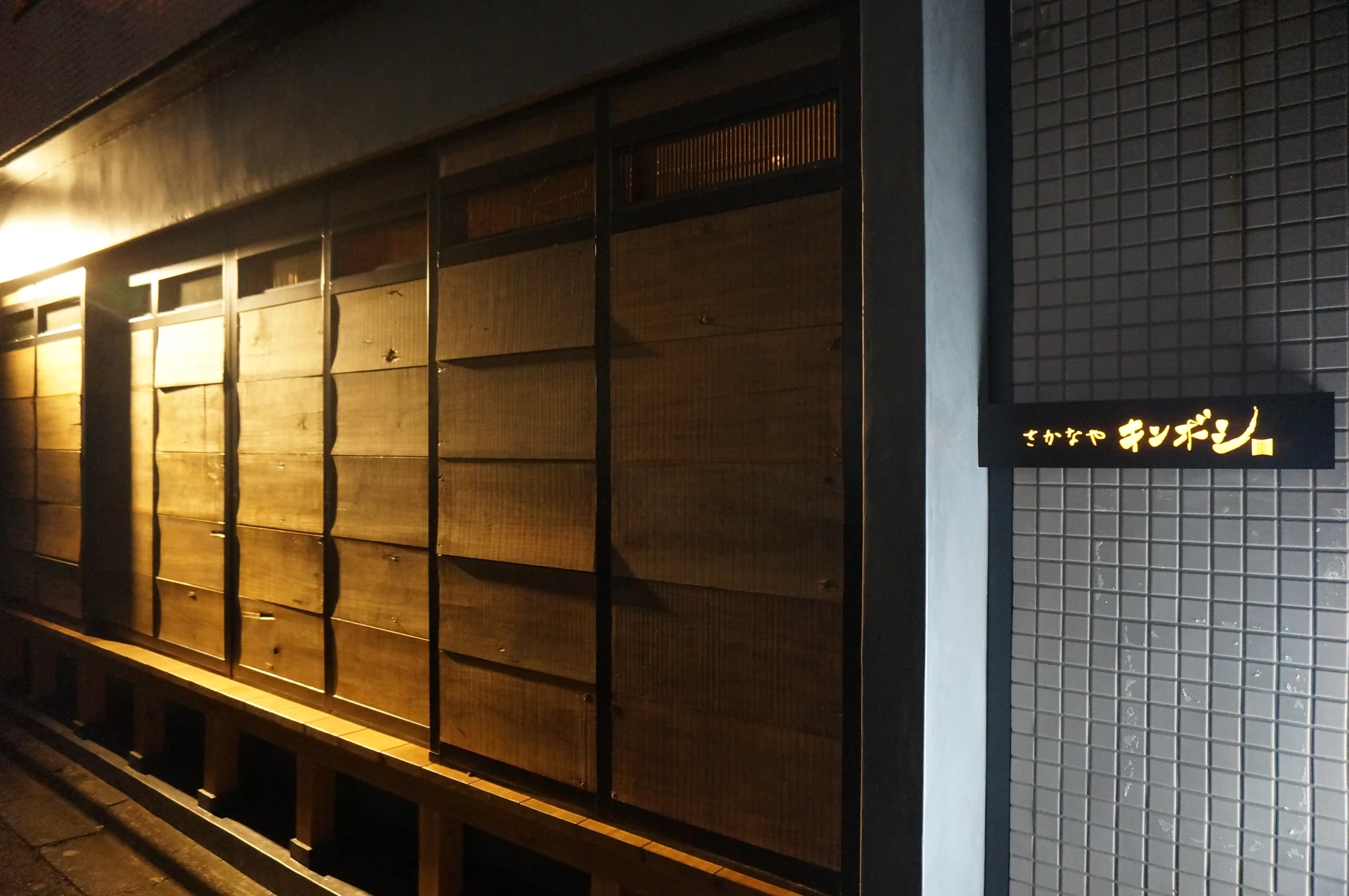 木の外壁に灯る「さかなや キンボシ」の看板