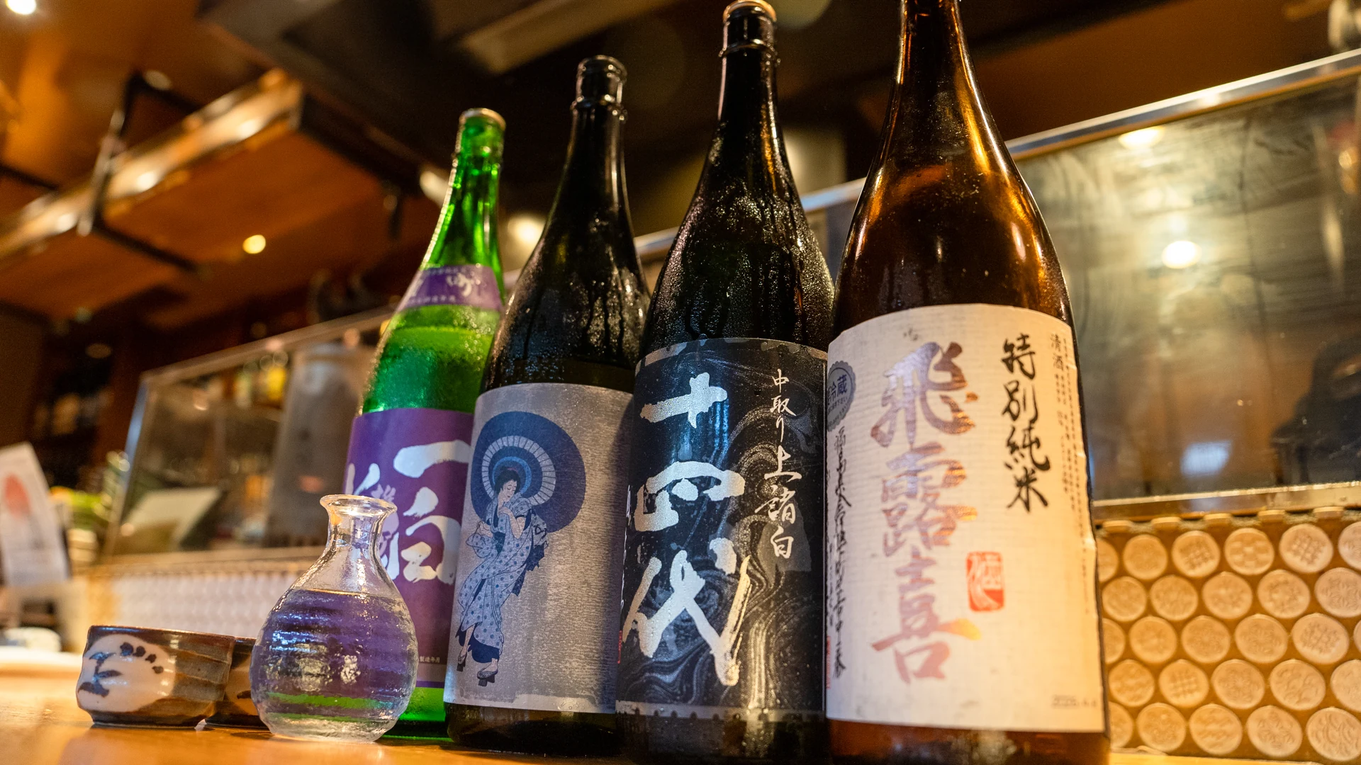 木のカウンターに並ぶ日本酒の瓶。取り扱い銘柄は時季により異なります